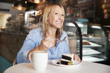 Woman In Coffee Shop Sitting At Table Eating Slice Of Cake