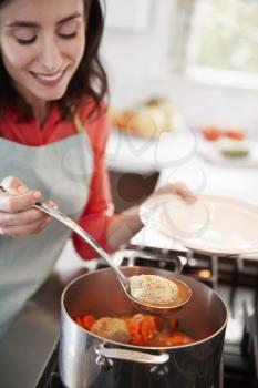 Woman serving Jewish matzon ball soup from a pot on the hob