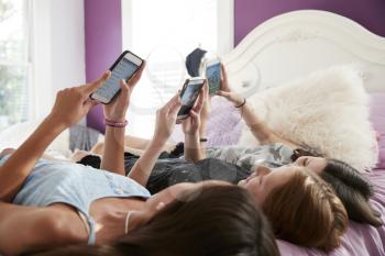 Three teenage girls lying on bed using smartphones, close up