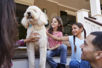 Family With Dog Sitting On Steps Of New Home On Moving In Day