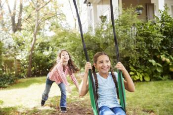 Two Sisters Having Fun On Garden Swing At Home