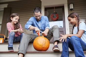 Father And Daughters Carving Halloween Pumpkin On House Steps