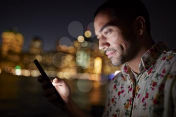 Man Using Mobile Phone At Night With City Skyline In Background