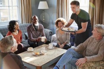 Waiter Serving Group Of Mature Friends In Coffee Shop