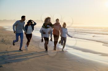 Group Of Friends Having Fun Running Along Winter Beach Together