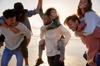 Group Of Friends Having Piggyback Race On Winter Beach Together