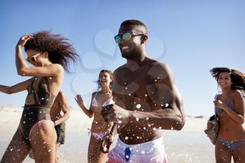 Group Of Friends Run Through Waves Together On Beach Vacation