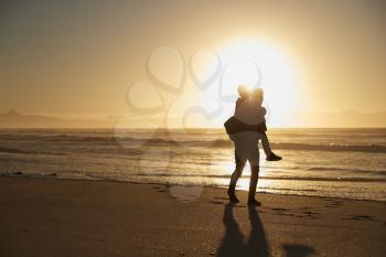 Silhouette Of Father Giving Son Piggyback On Winter Beach