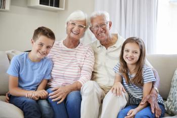 Portrait Of Grandchildren Sitting On Sofa With Grandparents