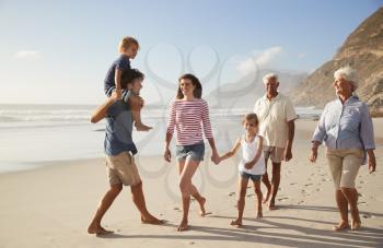 Multi Generation Family On Vacation Walking Along Beach Together