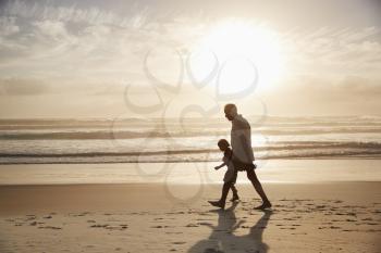 Silhouette Of Grandfather Walking Along Beach With Grandson