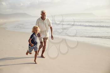 Grandfather Running Along Beach With Grandson On Summer Vacation
