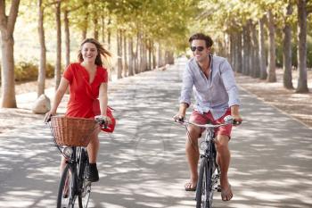 Young white adult couple riding bikes on a tree lined road
