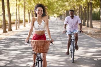 Young mixed race couple riding bicycles on a tree lined road