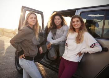 Three female friends on road trip looking at camera from car