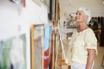 Senior Woman Looking At Paintings In Art Gallery