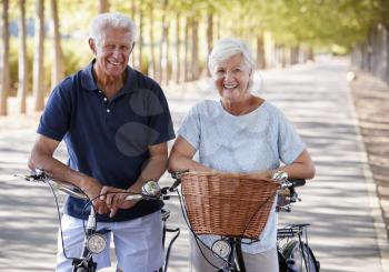 Portrait Of Smiling Senior Couple Cycling On Country Road