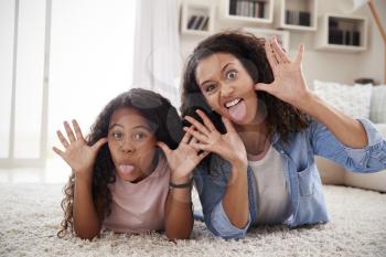 Mother And Daughter Lying On Rug And Pulling Faces At Home