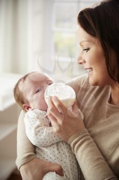 Mother Feeding Newborn Baby From Bottle At Home