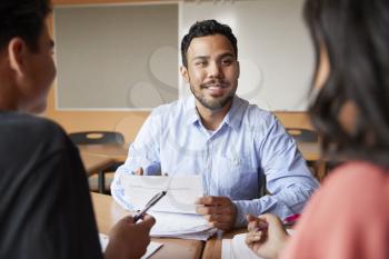 Male High School Tutor With Two Students At Desk In Seminar