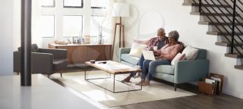 Senior Couple Sitting On Sofa At Home Using Laptop To Shop Online