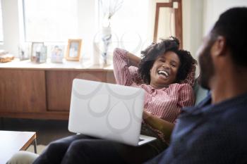 Couple Sitting On Sofa At Home With Woman Using Laptop Computer