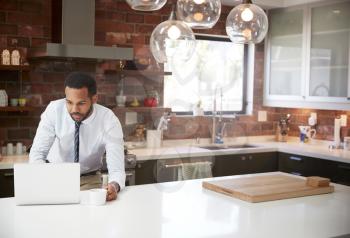 Businessman Using Laptop On Kitchen Island Before Leaving For Work