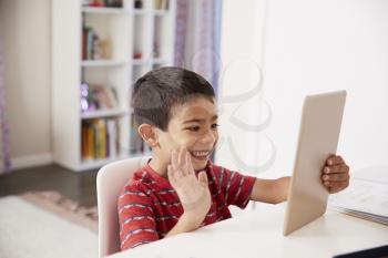 Young Boy Sitting At Desk In Bedroom Using Digital Tablet To Make Video Call
