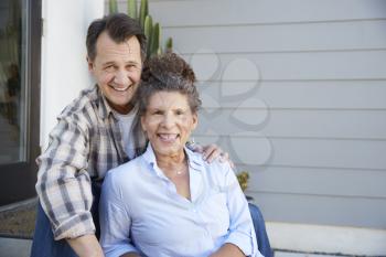 Portrait Of Senior Couple Sitting Outside Grey Clapboard House