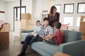 Happy Family Resting On Sofa Surrounded By Boxes In New Home On Moving Day