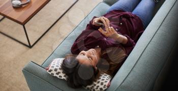 Overhead View Of Woman Lying On Sofa At Home Using Mobile Phone