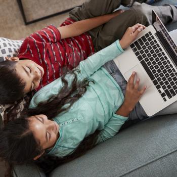 Overhead View Of Brother And Sister Sitting On Sofa At Home Having Fun Playing On Laptop Together