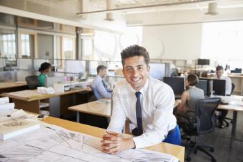 Young male architect in busy office smiling to camera