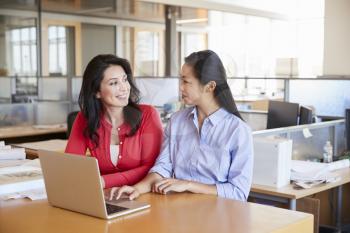 Two female architects using a laptop looking at each other