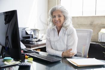 Senior woman sitting at desk in office smiling to camera