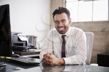 Young Hispanic businessman at office desk smiling to camera