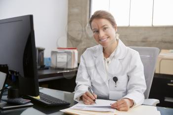 Young white female doctor at desk in office, portrait
