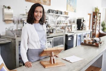 Female coffee shop owner standing smiling behind the counter