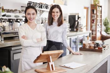 Two female coffee shop owners smiling behind counter