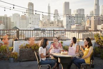 Female Friends Celebrating Birthday On Rooftop Terrace With City Skyline In Background