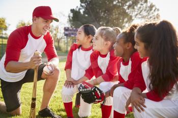 Girl baseball team kneeling in a huddle with their coach