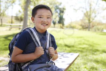Young Asian schoolboy with backpack smiling to camera