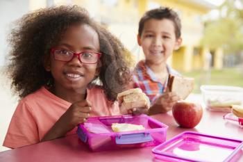 Two young school kids eating their packed lunches together