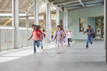 Elementary school kids running in school corridor, side view