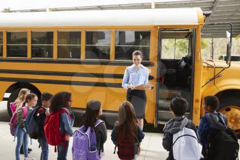 Teacher taking a register of school kids by school bus