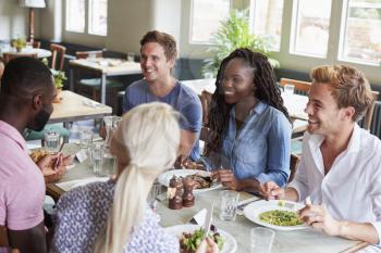 Group Of Friends Sitting At Table In Restaurant Enjoying Meal Together