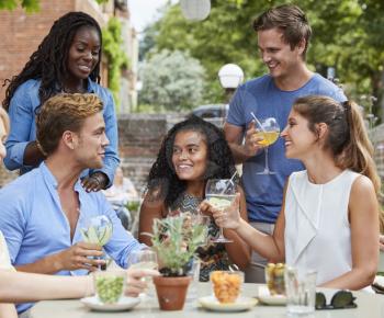 Friends Sitting At Table In Pub Garden Enjoying Drink Together