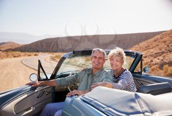 Senior couple smile to camera from parked open top car