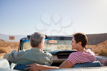 Father and adult son on road trip in open top car, back view