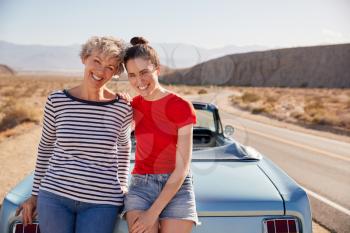 Mum and adult daughter on road trip leaning against the car